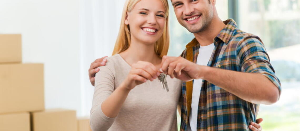 Keys of their new house. Cheerful young couple holding keys and smiling while standing in their new house
